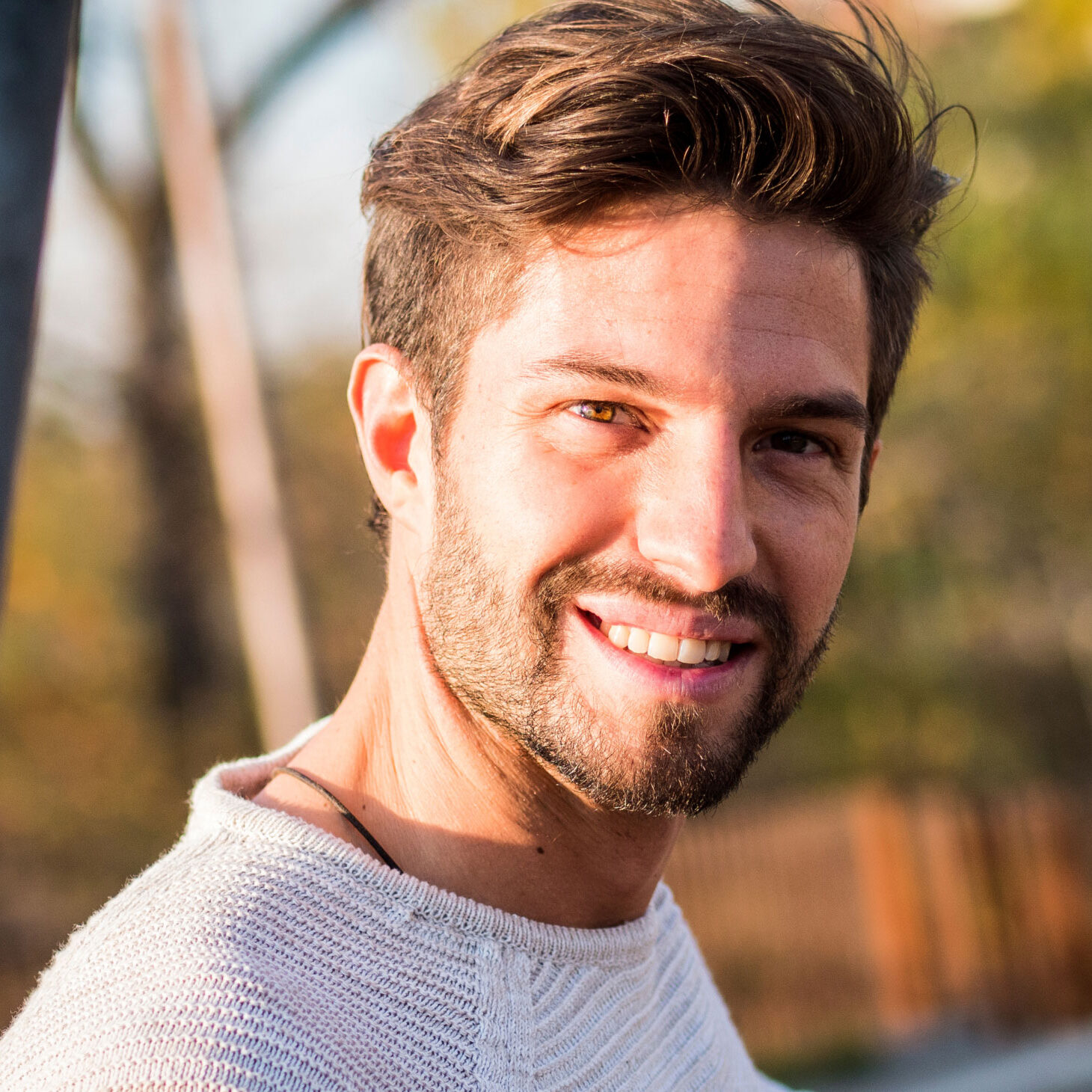 young man with beard smiling at the camera while on a walk in the park