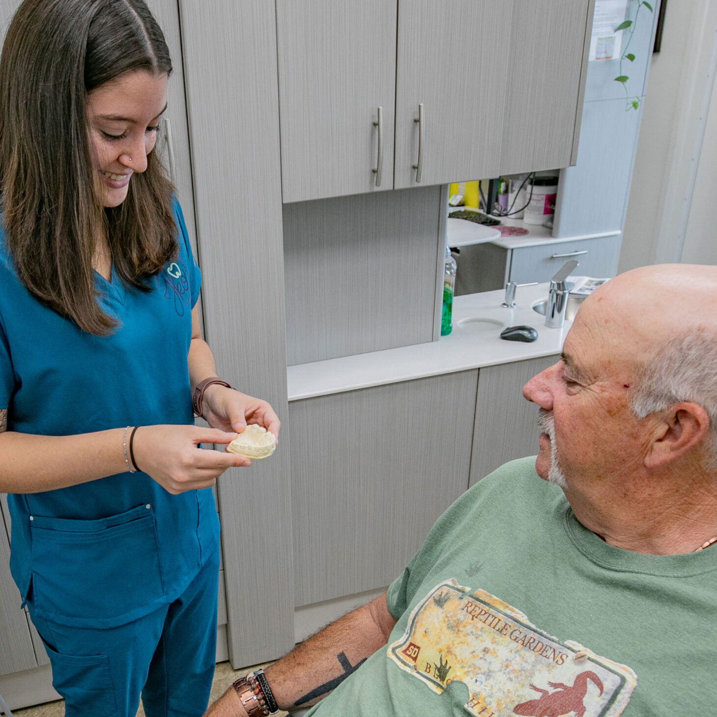 dental assistant using model of teeth to demonstrate a dental procedure to patient