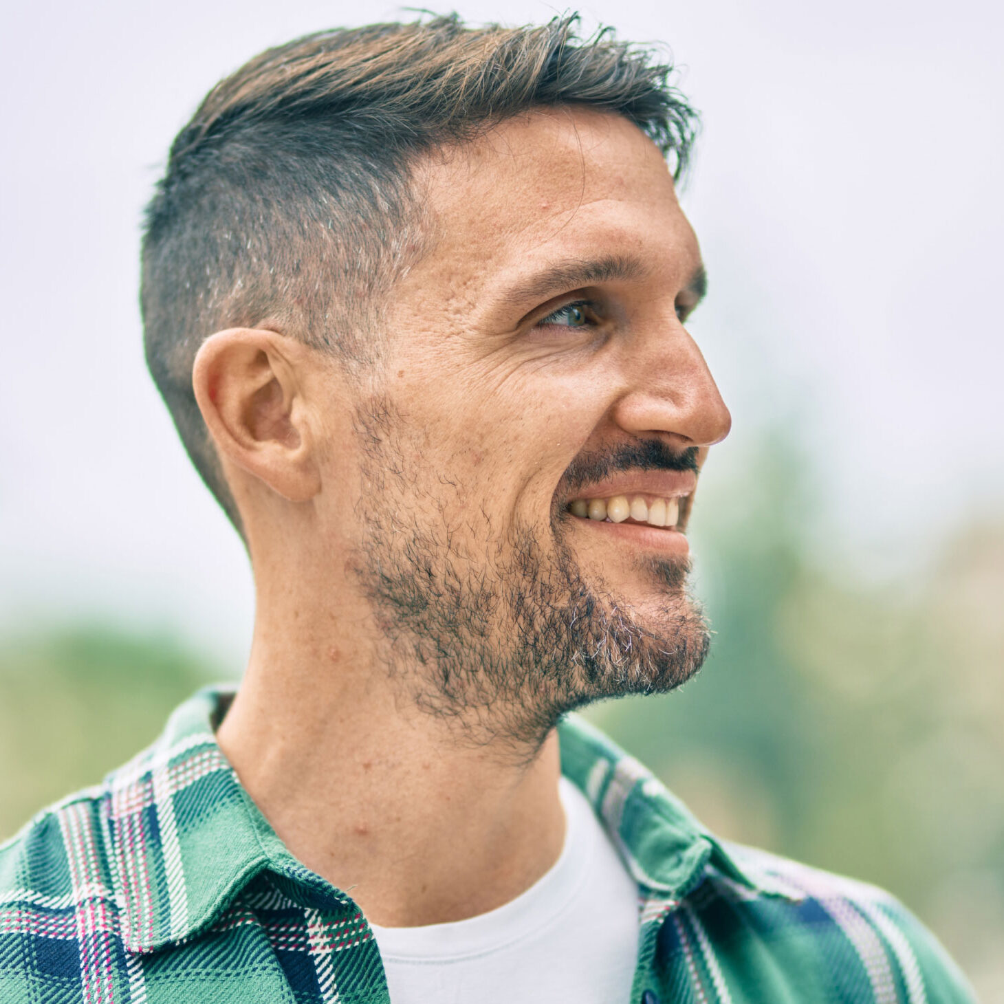 man wearing plaid shirt looking to the right and smiling